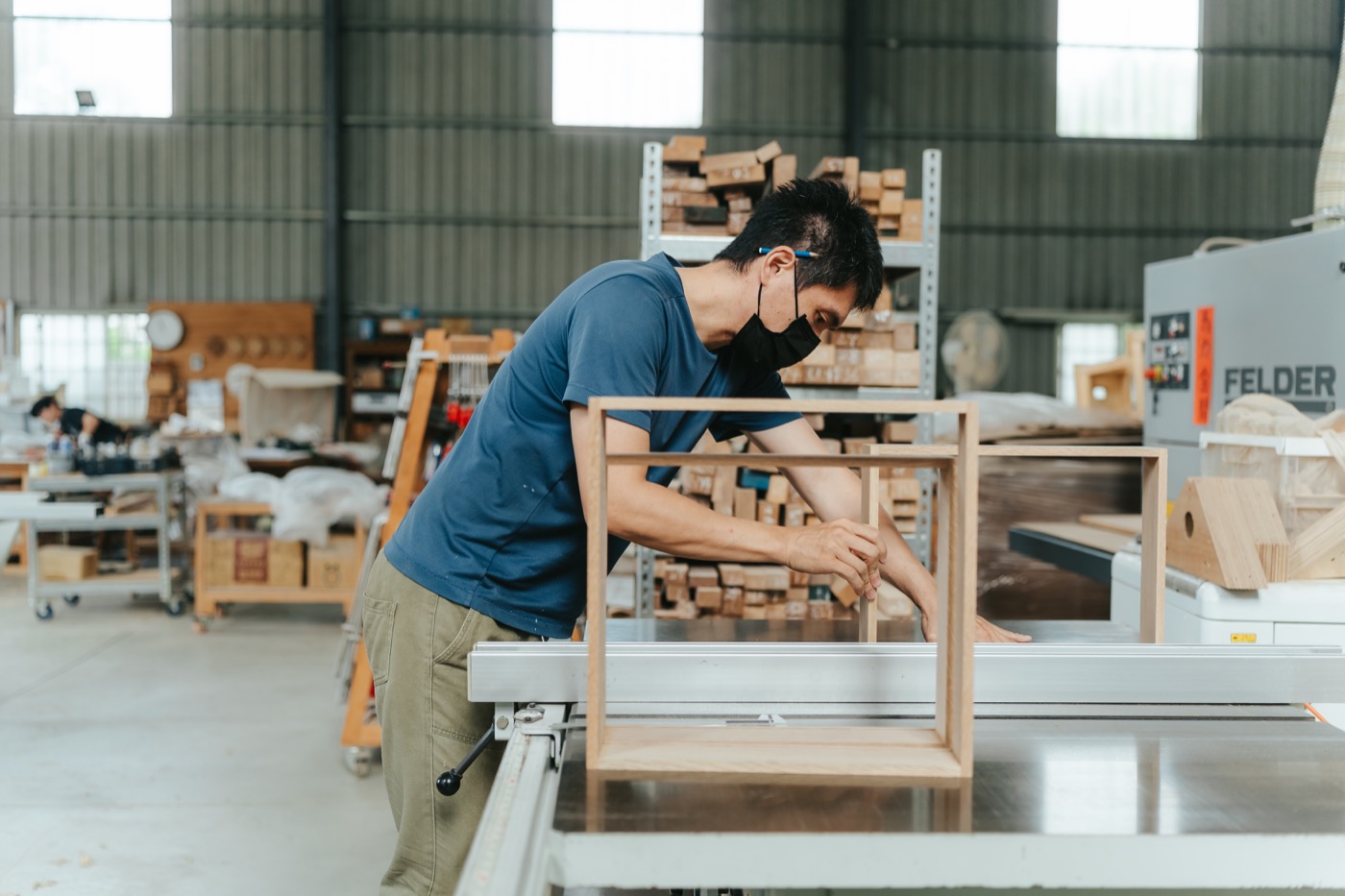 路力工作室內,製作者俯身處理工作台上的木製家具框架